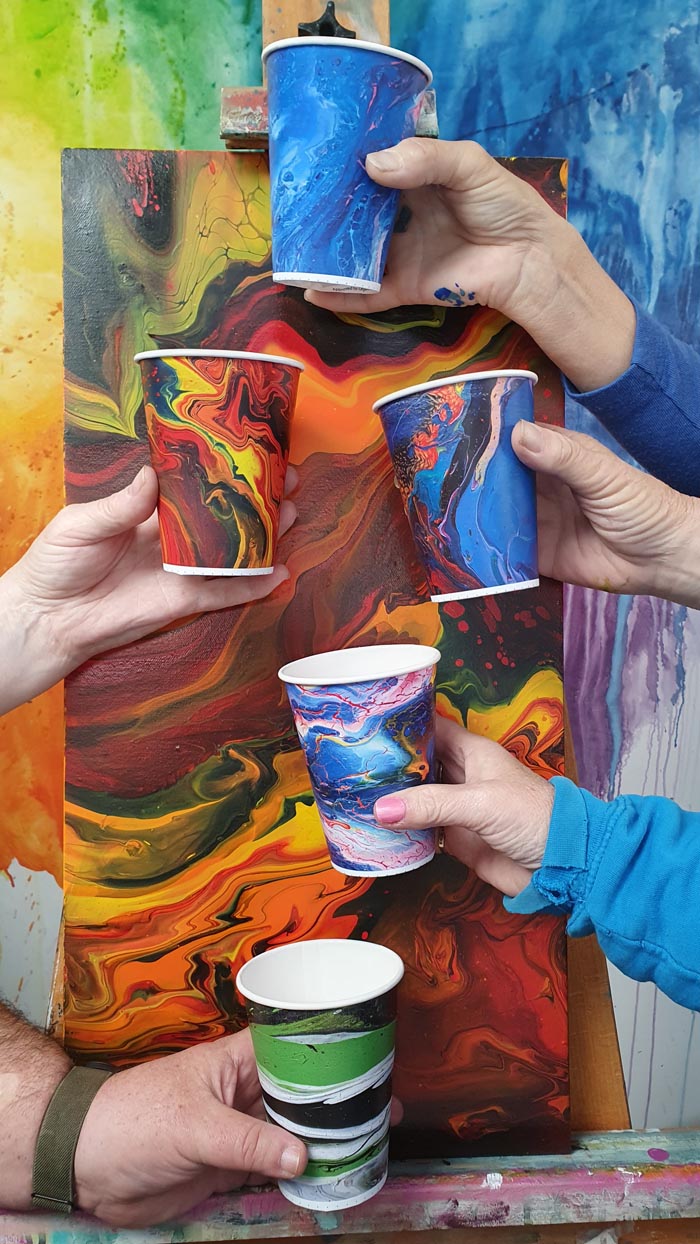 Hands hold five colourful disposable cups decorated with artwork